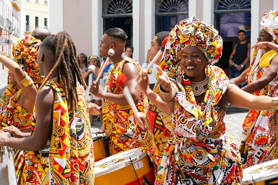 Pequeno desfile de dançarinos com trajes tradicionais celebrando com foliões o Carnaval nas ruas. Salvador, Bahia